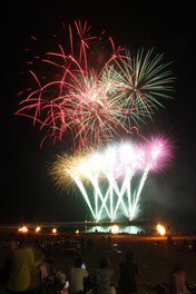 花火大会に先立ちたかれるビーチの篝火、赤い空中ナイアガラ、篝火と花火の競演が夜空を彩る